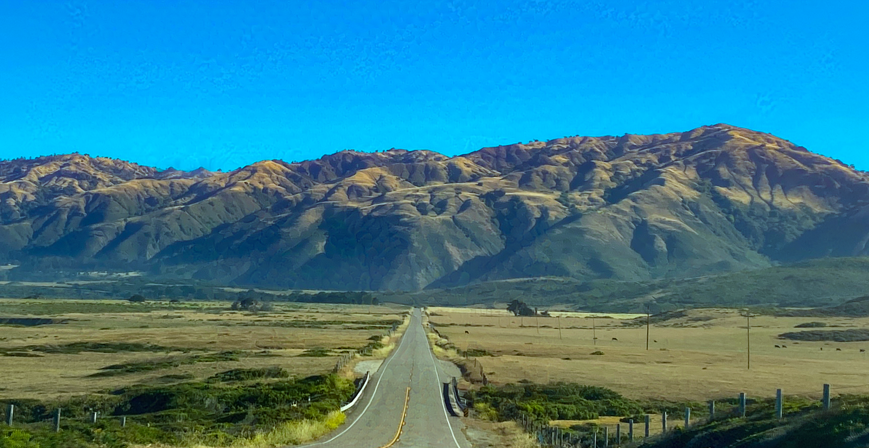 Straight road through golden hills toward coastal mountains